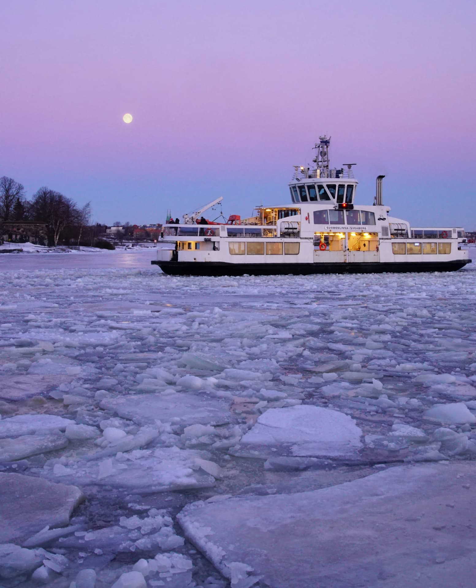 The Suomenlinna ferry pushing through drifting sea ice off Helsinki at dusk under a full moon