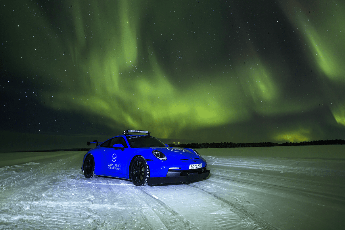 A blue sports car on a frozen lake ice-driving circuit in Lapland under green aurora