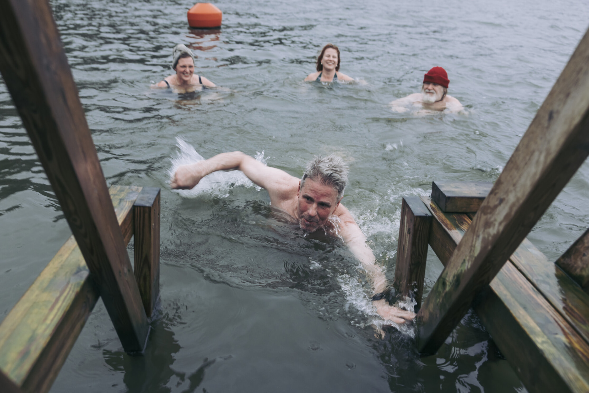 A group of winter swimmers in the sea beside a wooden jetty ladder in Helsinki