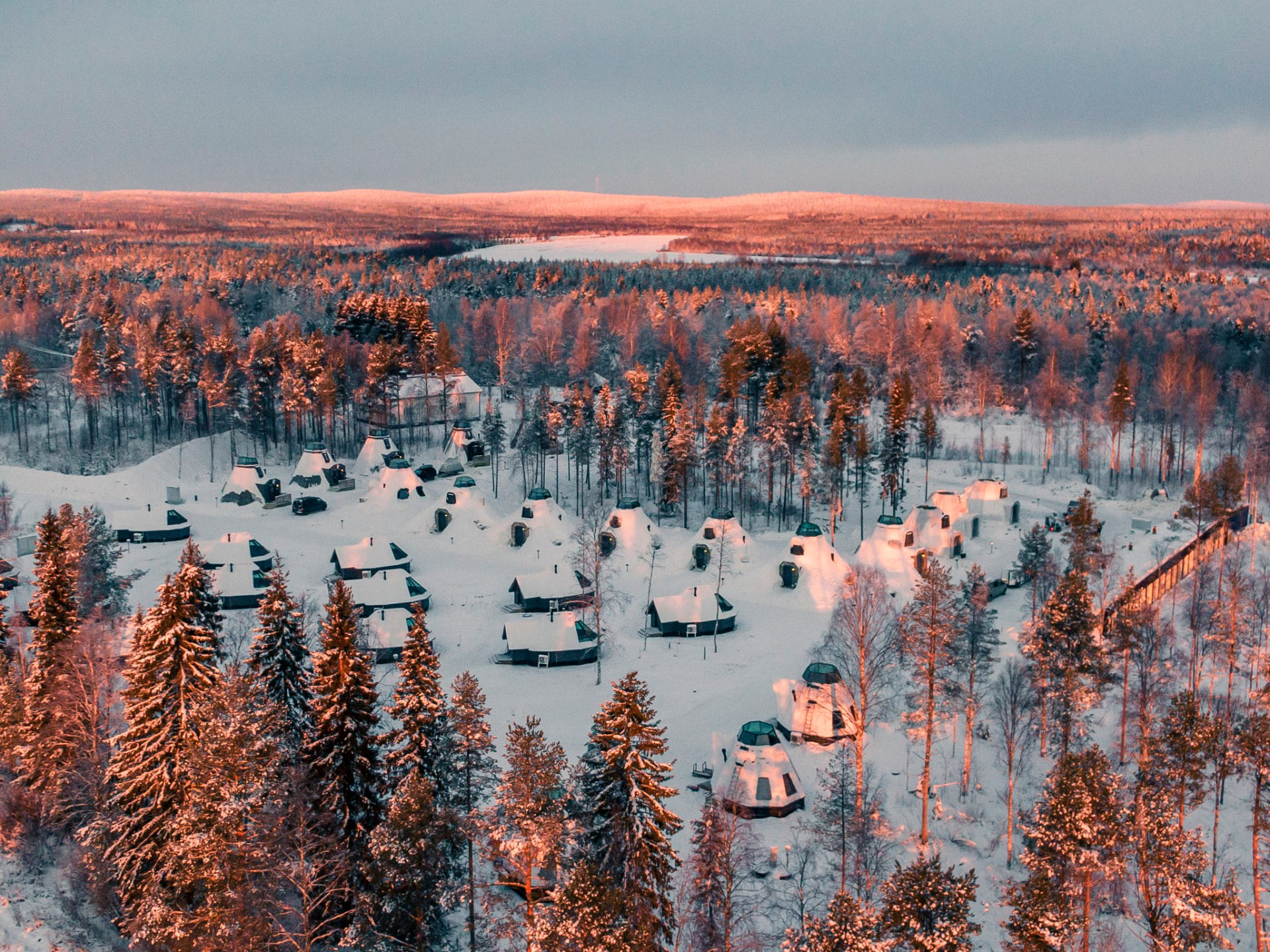 Aerial view of Apukka Resort's cabins and igloos in snowy forest at sunrise