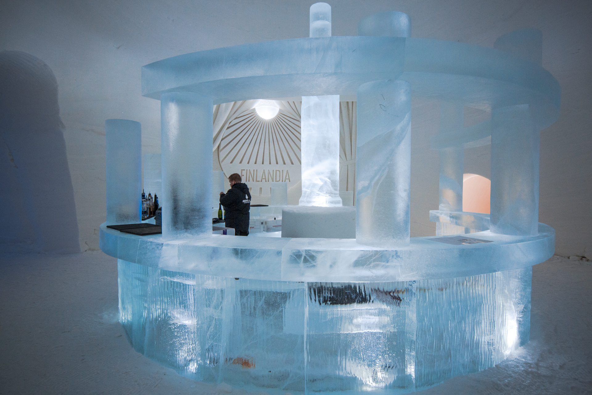 A circular bar carved entirely from ice, lit pale blue, in a snow hall in Finnish Lapland