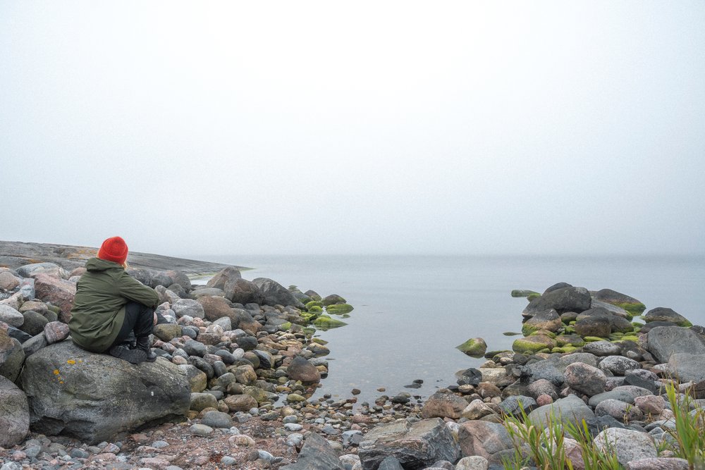 A lone figure on a boulder shore looking out over a fog-bound archipelago sea