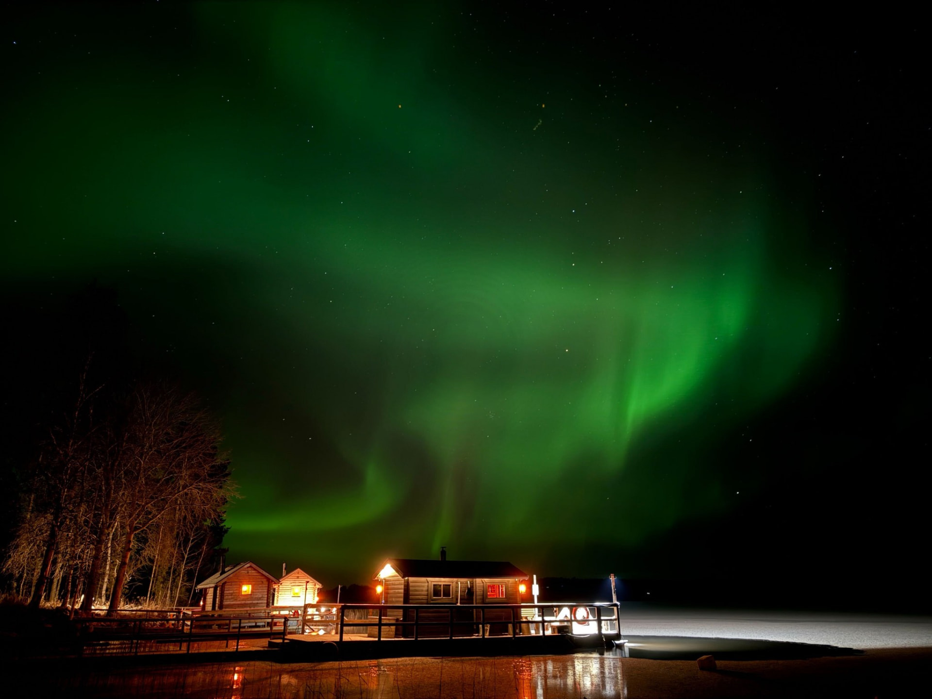 Apukka lakeside sauna glowing beneath a green aurora over the frozen lake