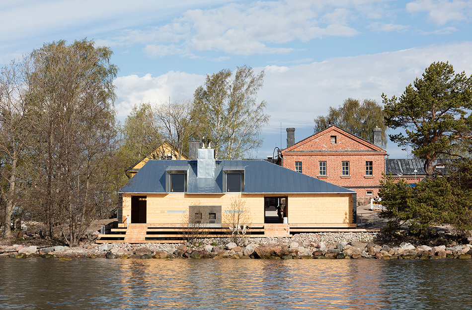 Wooden sauna building on the shore of a Helsinki island, with a red-brick building behind