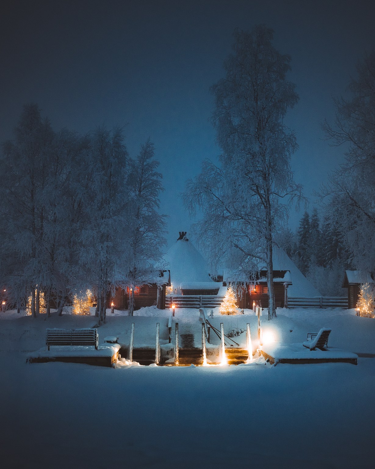 Lantern-lit lakeside sauna and ice pool at Apukka on a blue winter night