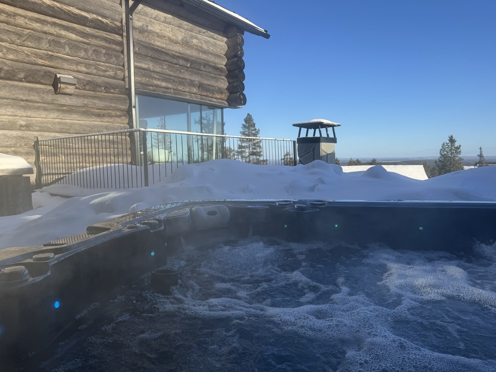 An outdoor hot tub on a villa terrace surrounded by deep snow under a clear arctic sky