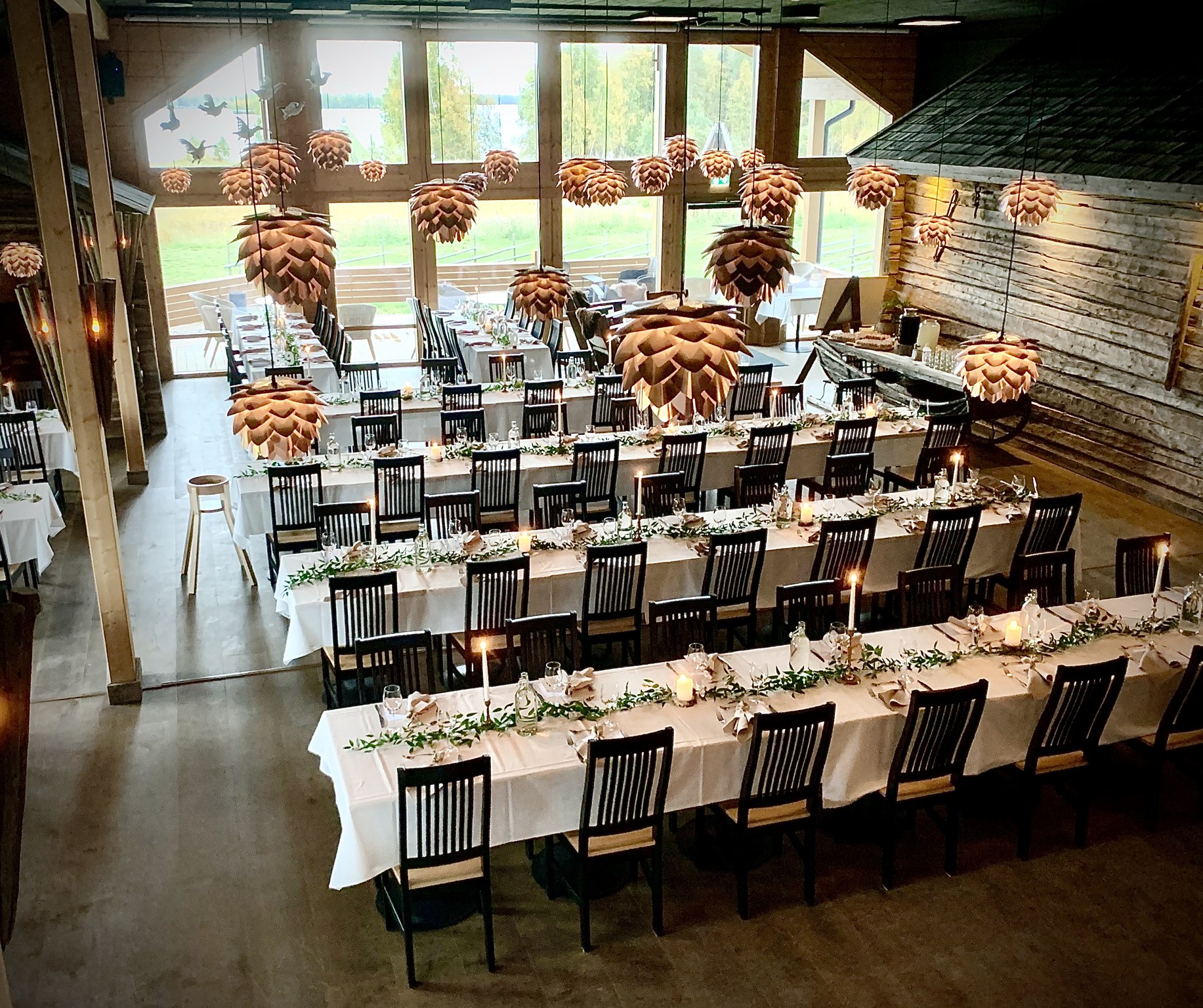 Long banquet tables set with candles and greenery in the timber Aitta hall