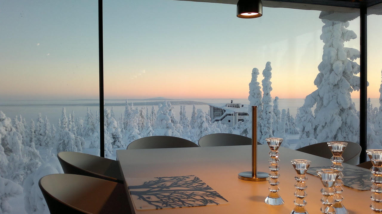 A dining table set beside a floor-to-ceiling window over snow-covered fells at dusk