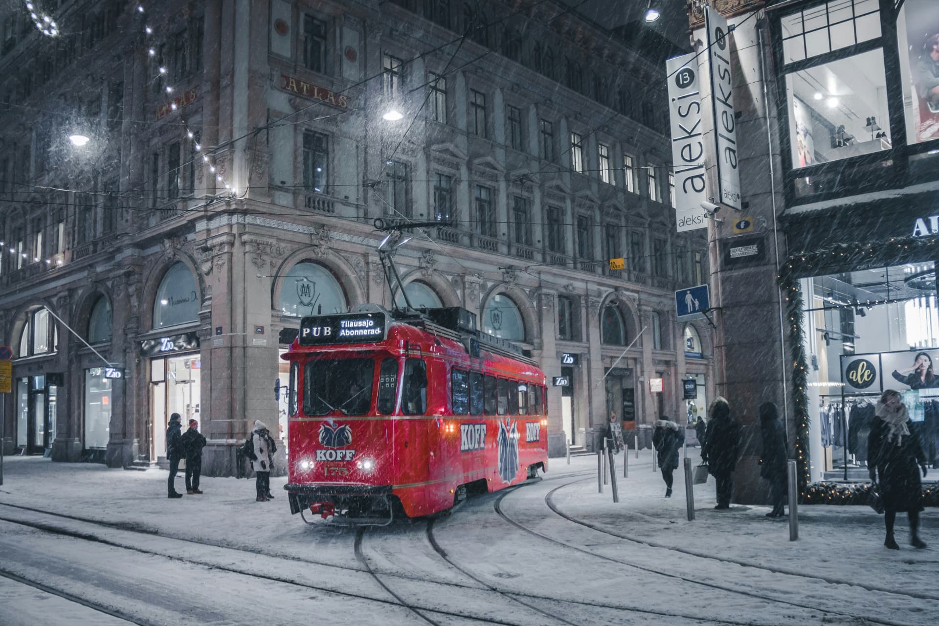 A red heritage tram on a snowy Helsinki street corner during evening snowfall