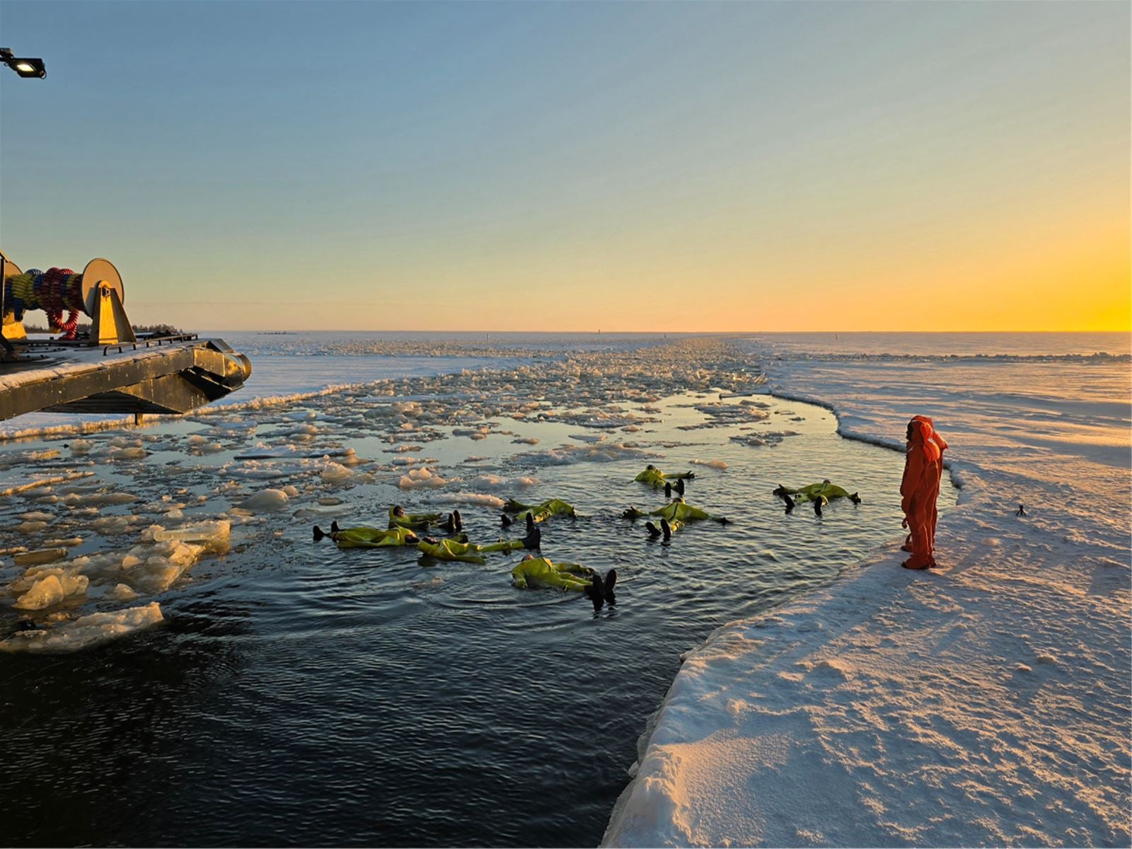 Guests in survival suits floating in the open channel beside the icebreaker at sunset