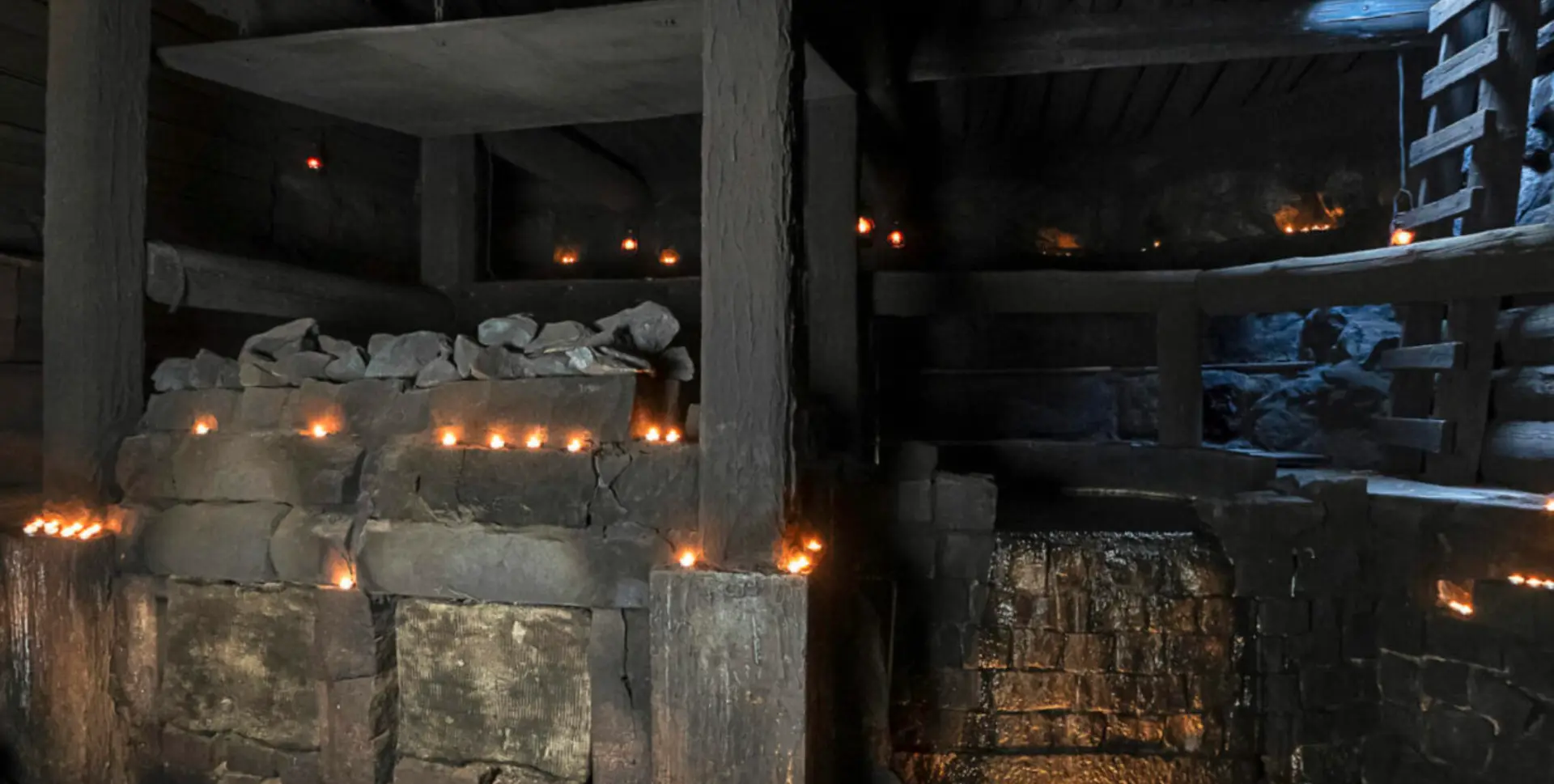 Candlelit underground smoke sauna with stone walls and timber beams