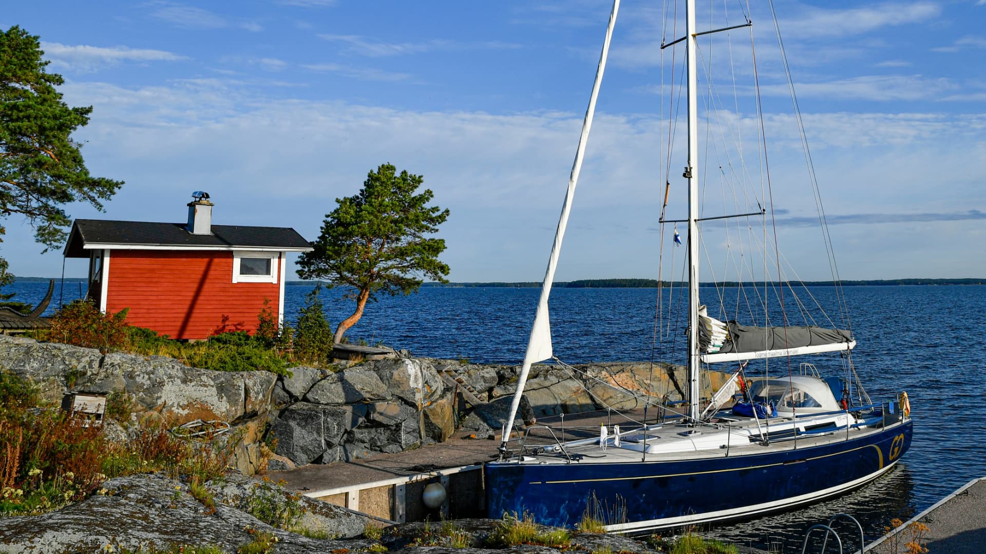 A red shore sauna on granite beside a moored sailing yacht in the Finnish archipelago