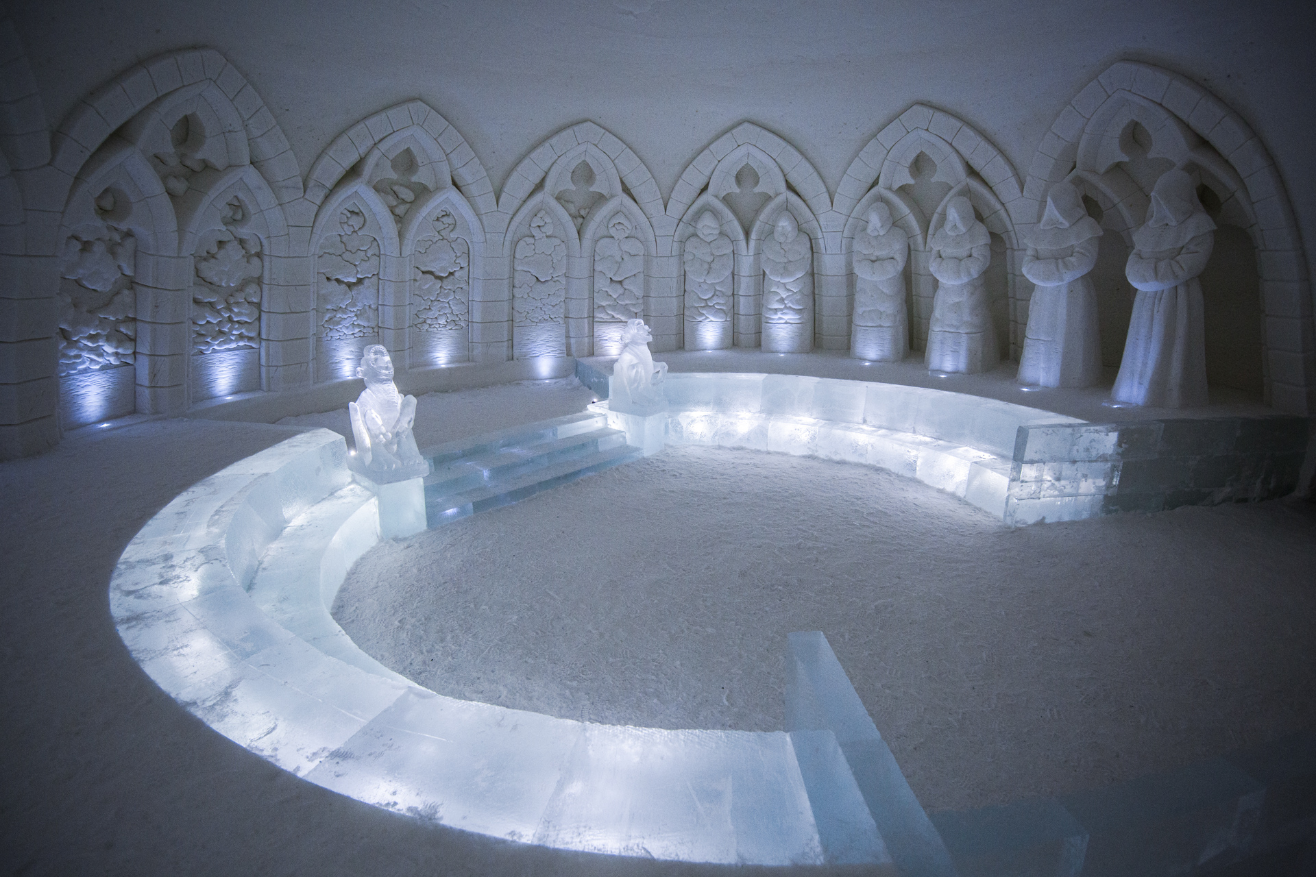 A snow chapel in Lapland with carved arches and a lit curved ice bench encircling the floor